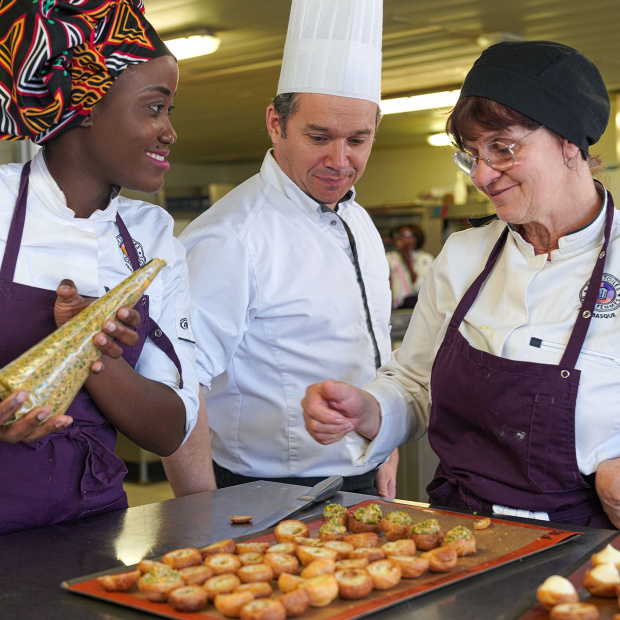 un chef en toque entouré de deux femmes préparant des desserts 