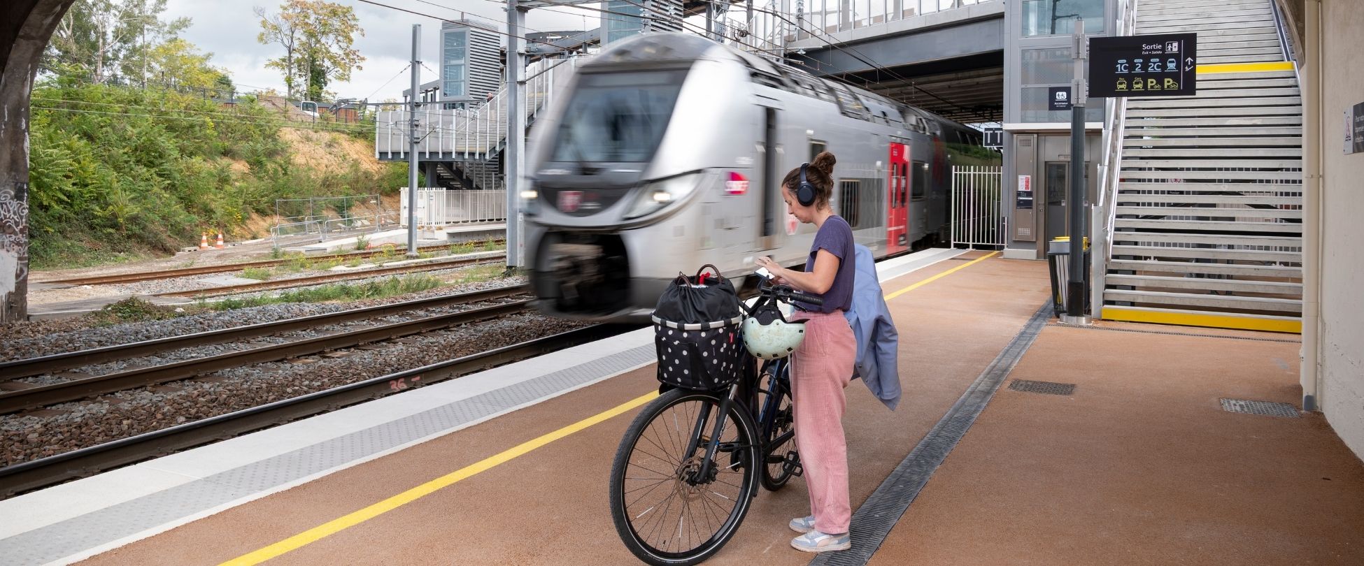 une personne avec son vélo attendant le train qui rentre en gare