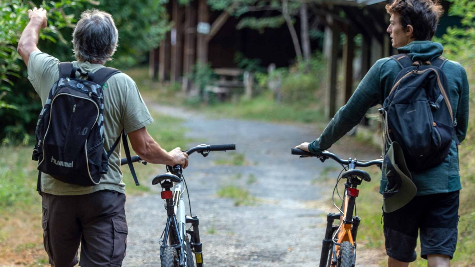 deux hommes poussant leur vélo sur un chemin forestier