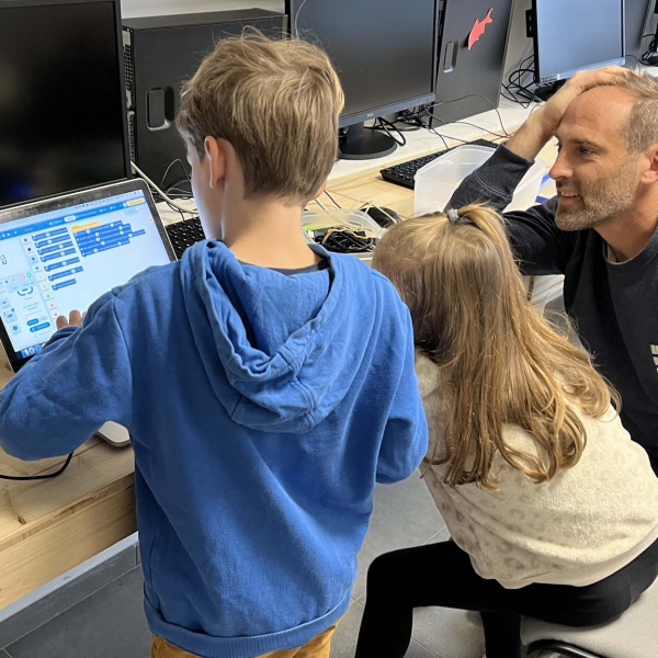 Deux enfants devant un ordinateur avec un adulte qui les regarde
